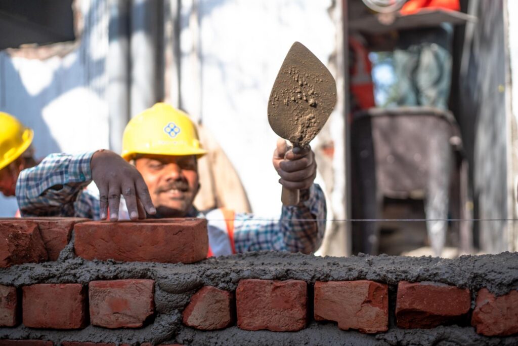 Masonry worker in a hard hat laying red brick in a fresh mortar bed with a trowel