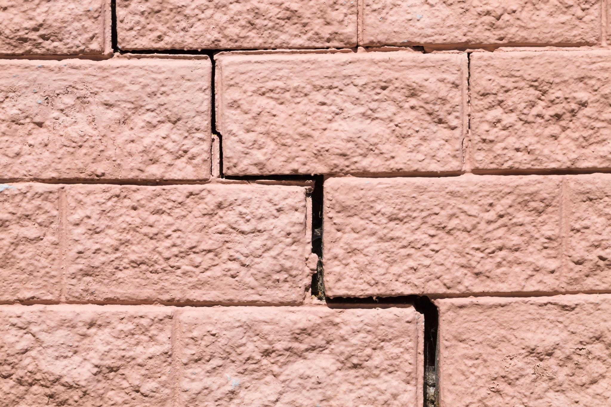 Stair-step crack running through the mortar joints of a painted brick wall, a sign masonry repair is needed