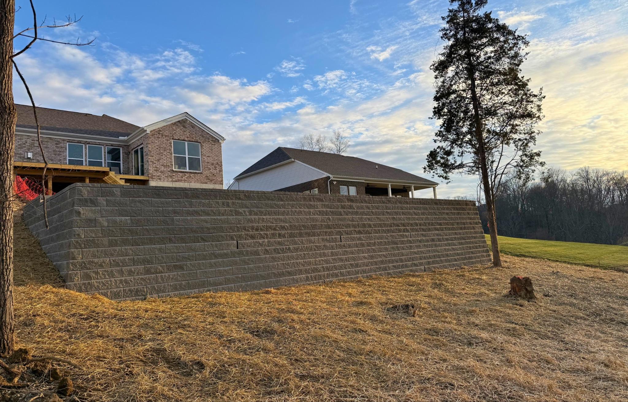 Tall engineered concrete block retaining wall terracing a slope behind newly built homes at dusk
