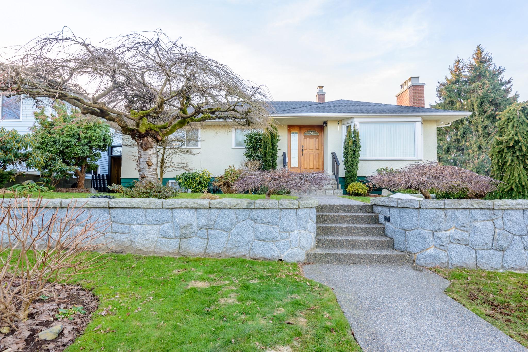 Single-story home fronted by a natural stone retaining wall with concrete steps and walkway